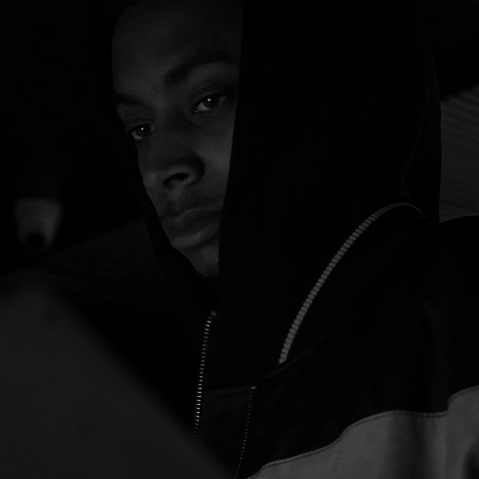 A young man with dark skin, wearing a hoodie, looking into the camera with a serious expression.