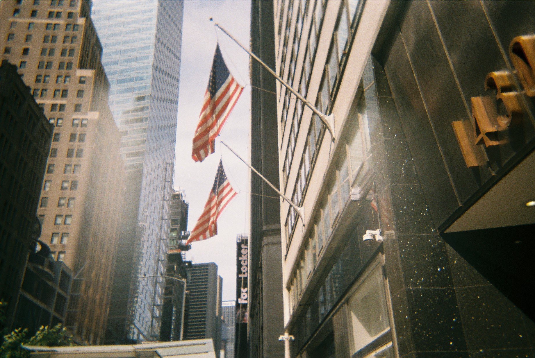 Multiple American flags hanging outside a tall building in a city, with skyscrapers in the background.