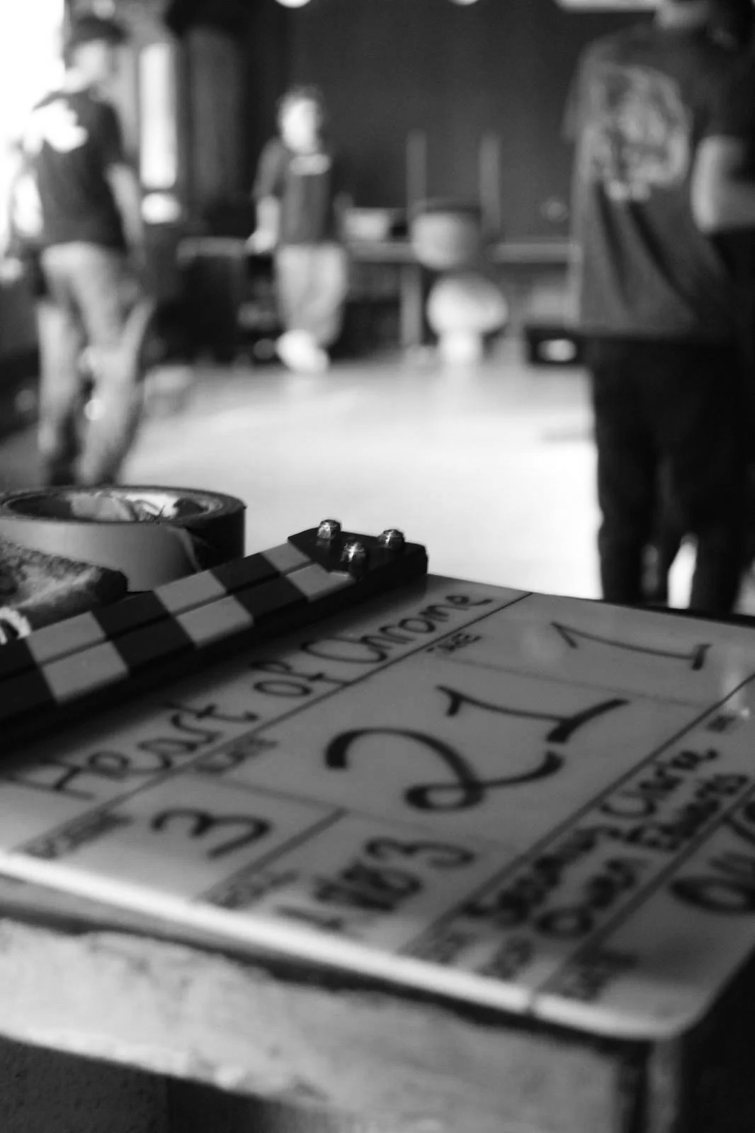 Close-up of a clapperboard with the words "Board of Directors" and "2" visible, placed on a table, with people and furniture blurred in the background.
