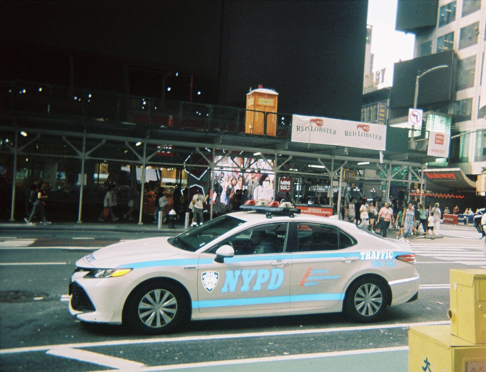 NYPD traffic police car parked on the street in a busy city area with pedestrians, tall buildings, and signs in the background.