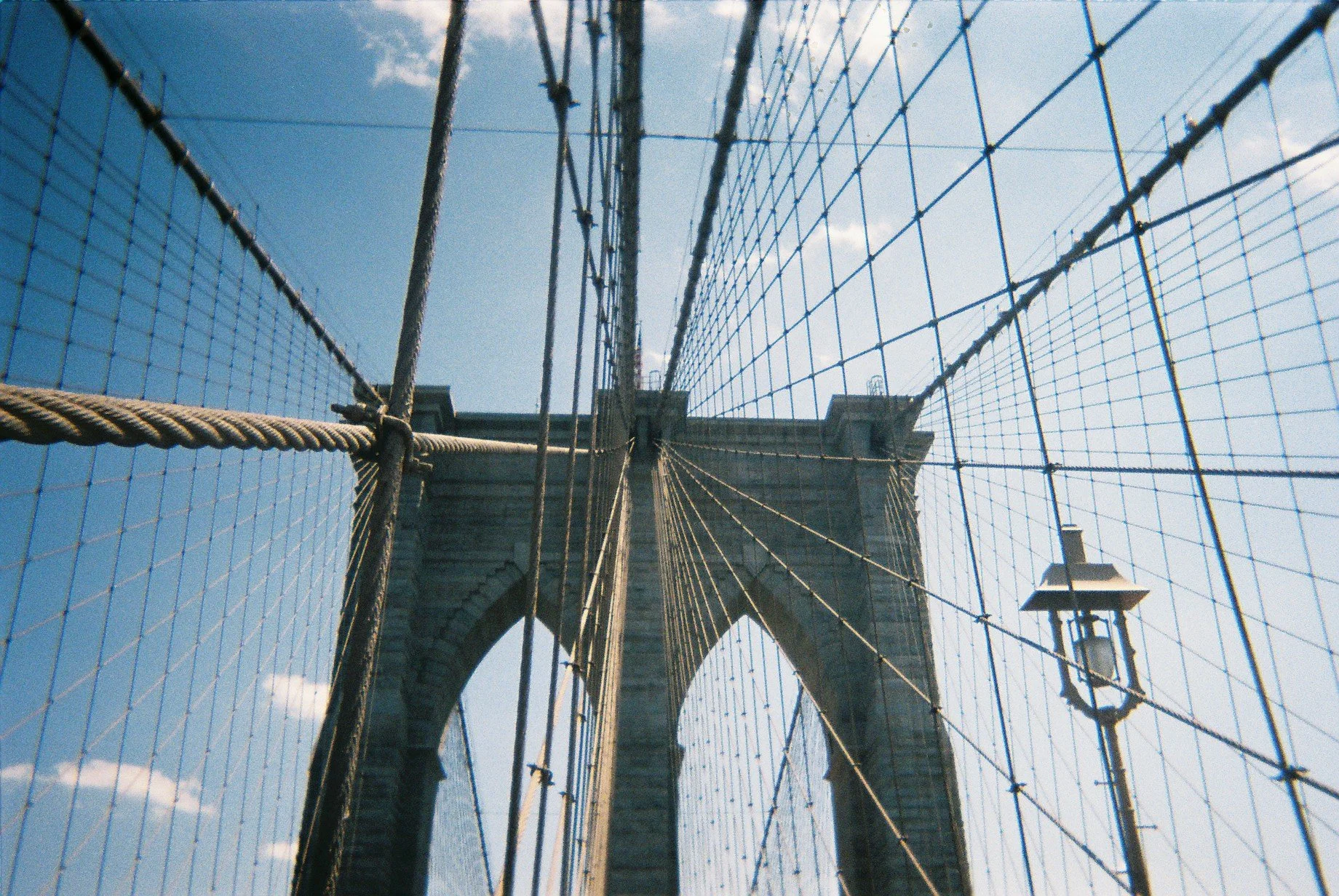 Looking up at the Brooklyn Bridge's stone towers and suspension cables against a blue sky.