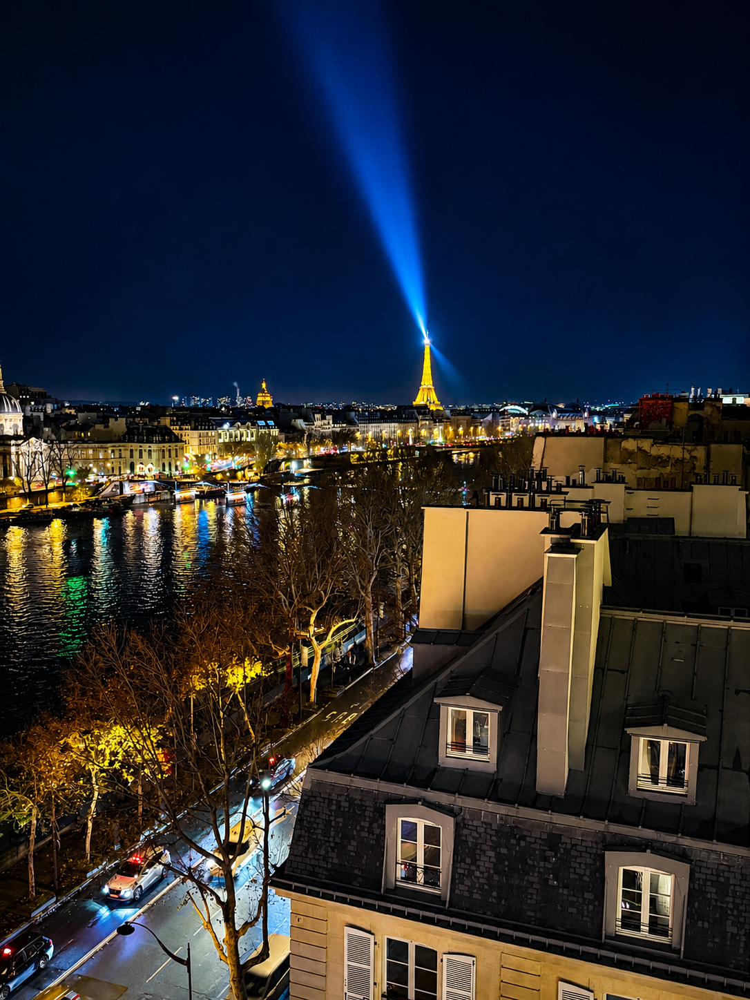 Nighttime view of Paris with illuminated Eiffel Tower, river, city lights, and buildings with rooftops in the foreground. Langosteria in Paris.