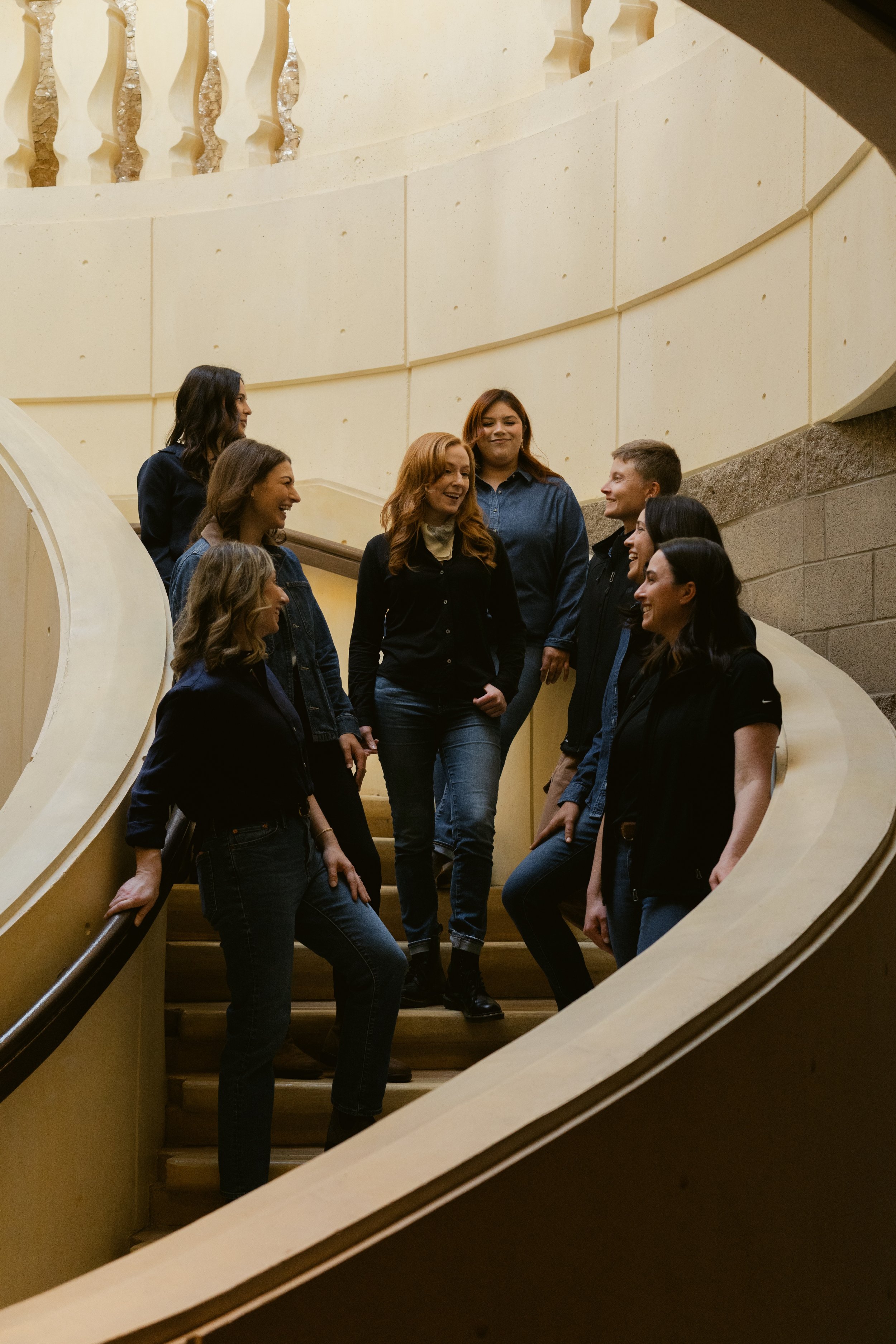 A group of women and one man standing on a staircase, smiling and engaging in conversation, viewed through a circular opening in the wall. Opus One Winery in Napa.