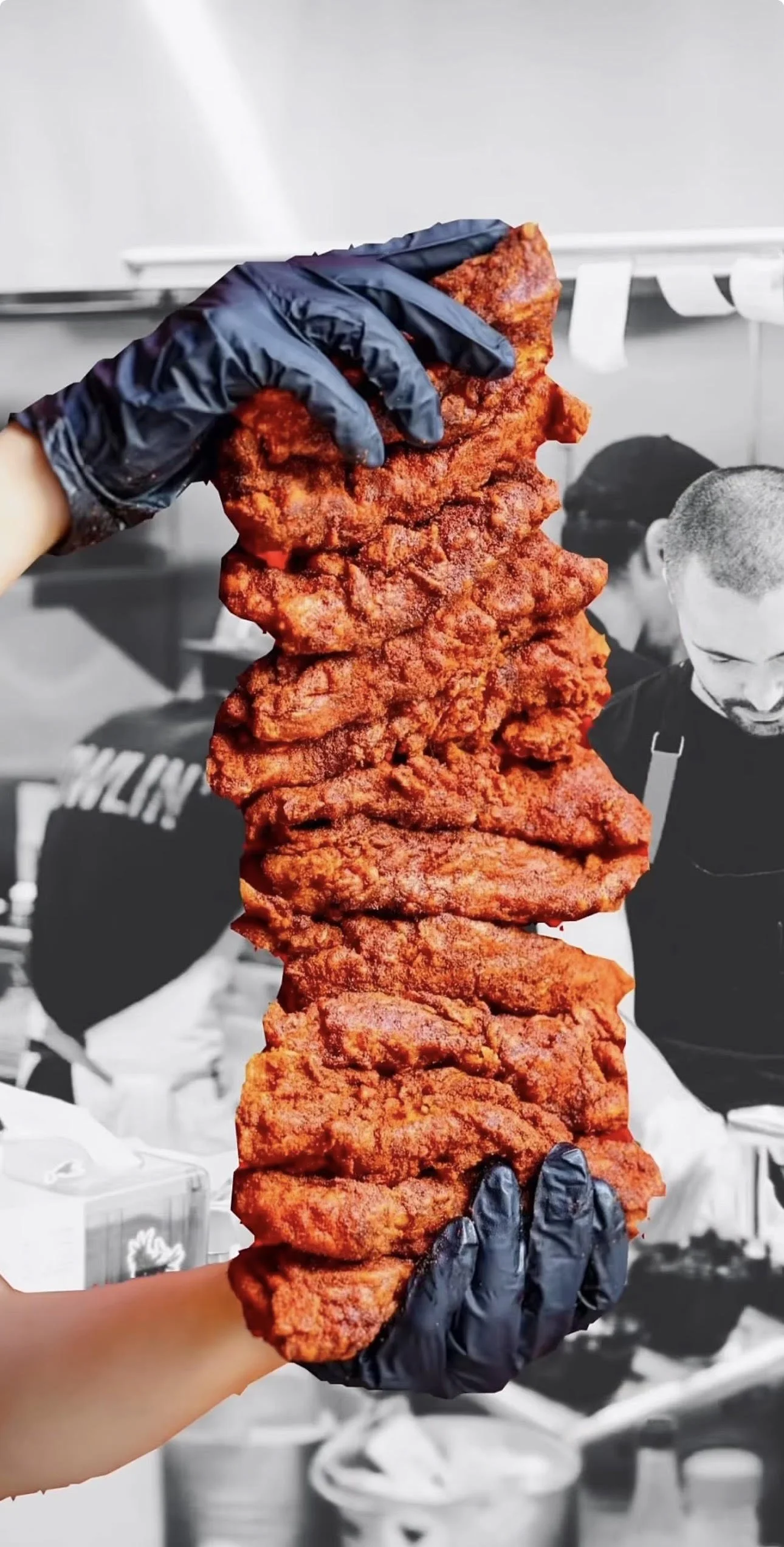 Person wearing black gloves holding a large stack of fried chicken. Howlin' Rays in Los Angeles.