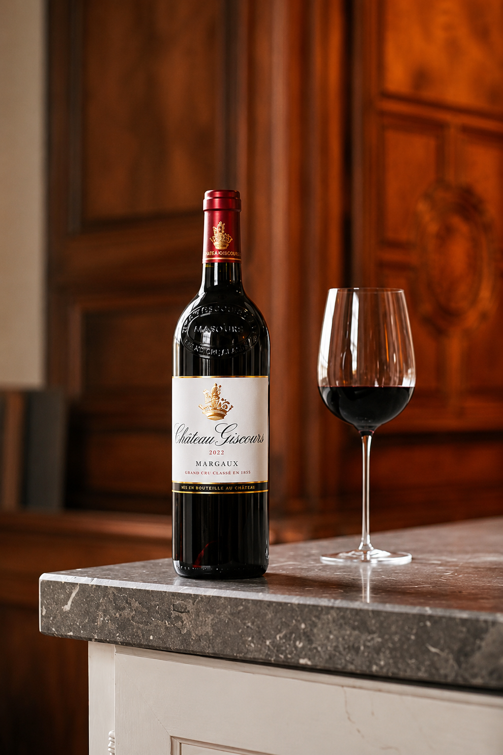 A bottle of Chateau Giscours Margaux wine from 2022 and a glass of red wine on a marble countertop with a wooden cabinet background.