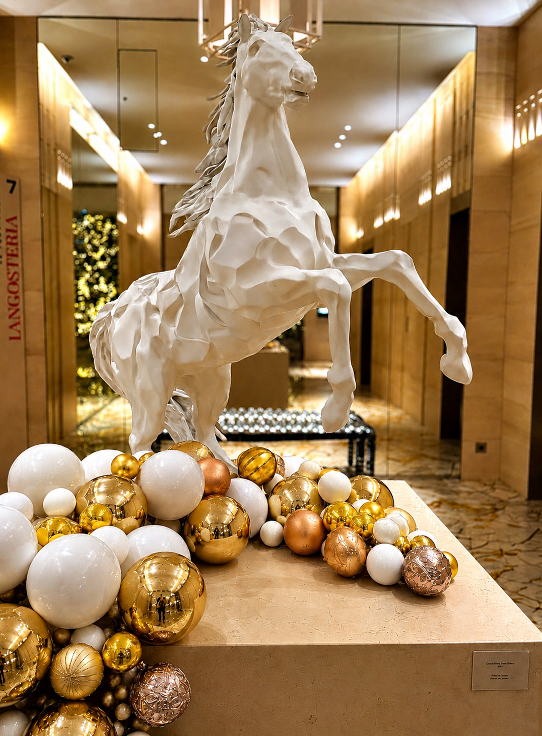 A white sculpture of a rearing horse displayed on a table decorated with gold, white, and bronze Christmas ornaments in an elegant, well-lit interior.  Langosteria in Paris.