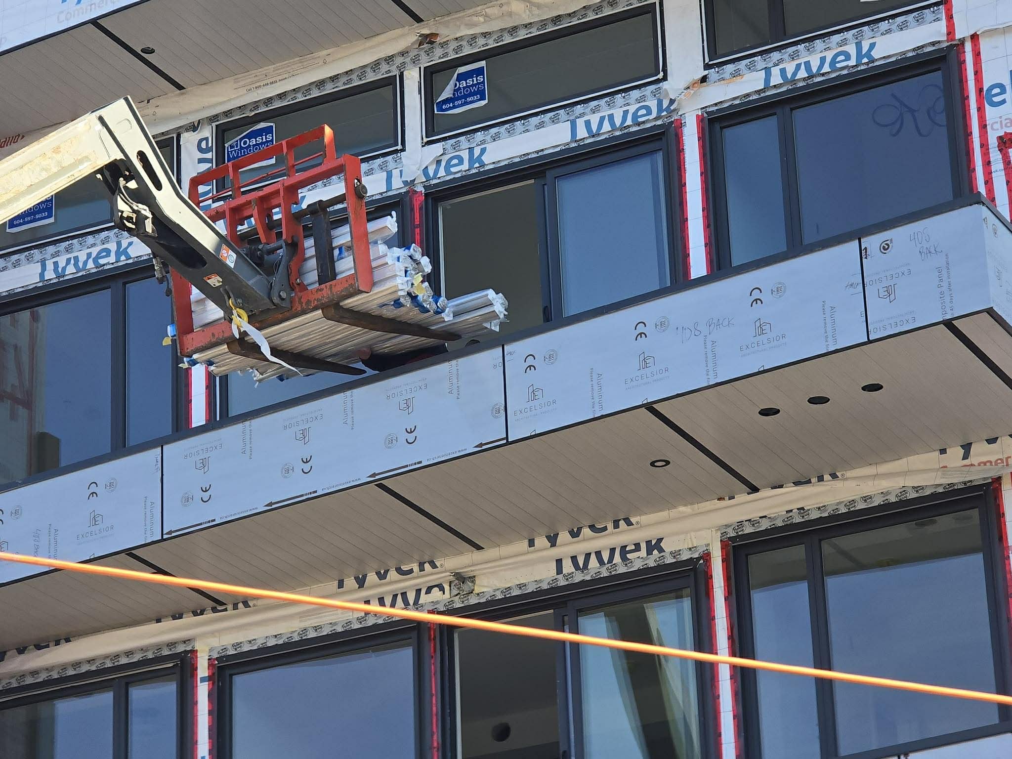 Construction site with a building featuring large windows, drywall panels, and a cherry picker lift.