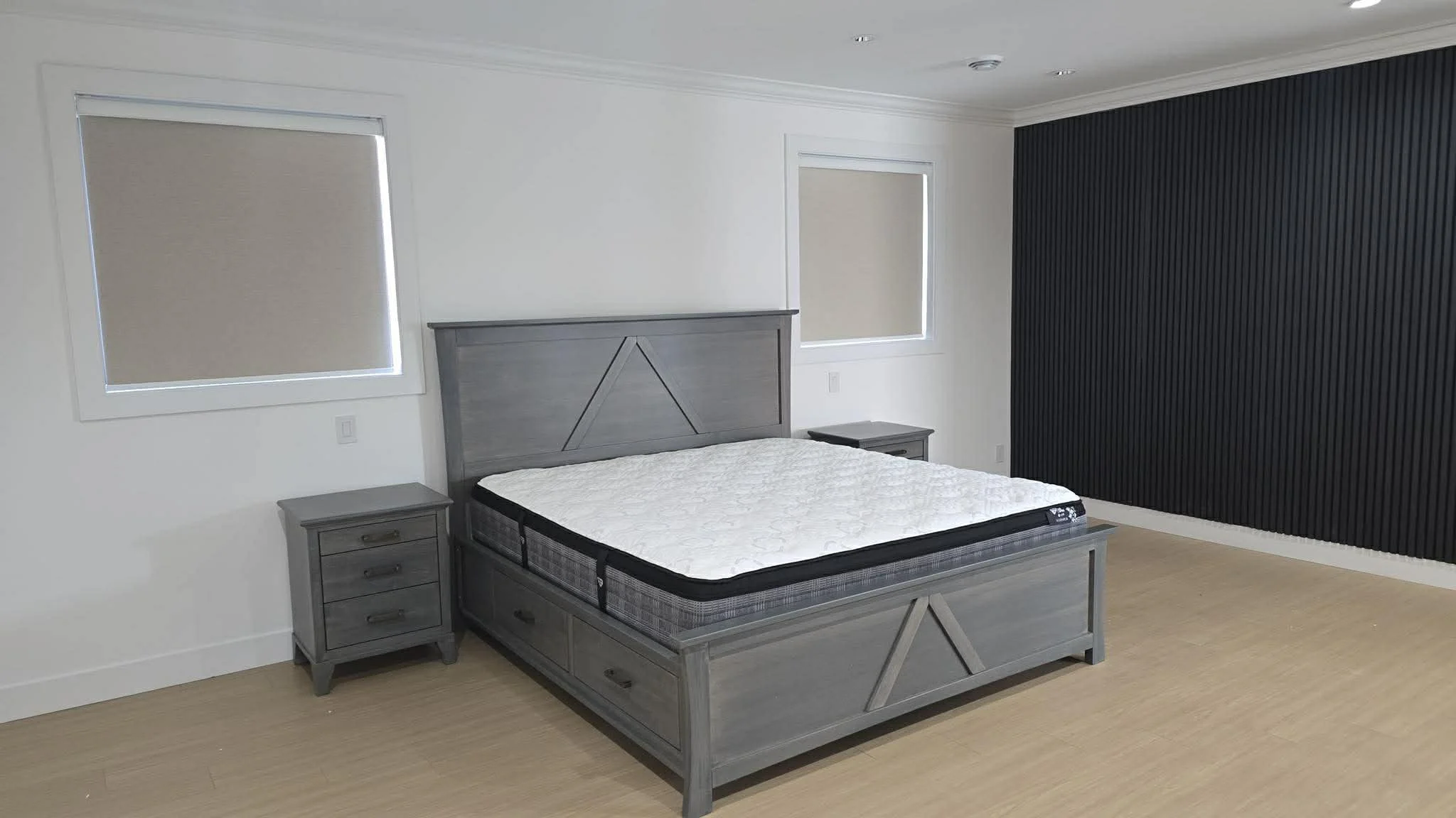 Empty bedroom with a gray wooden bed frame and mattress, two matching gray nightstands, and a black textured accent wall.
