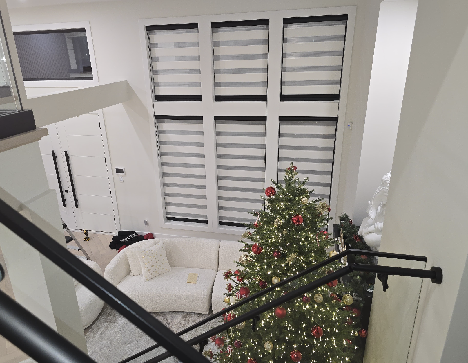 Decorated Christmas tree with red and gold ornaments and string lights in a modern living room, viewed from the staircase.