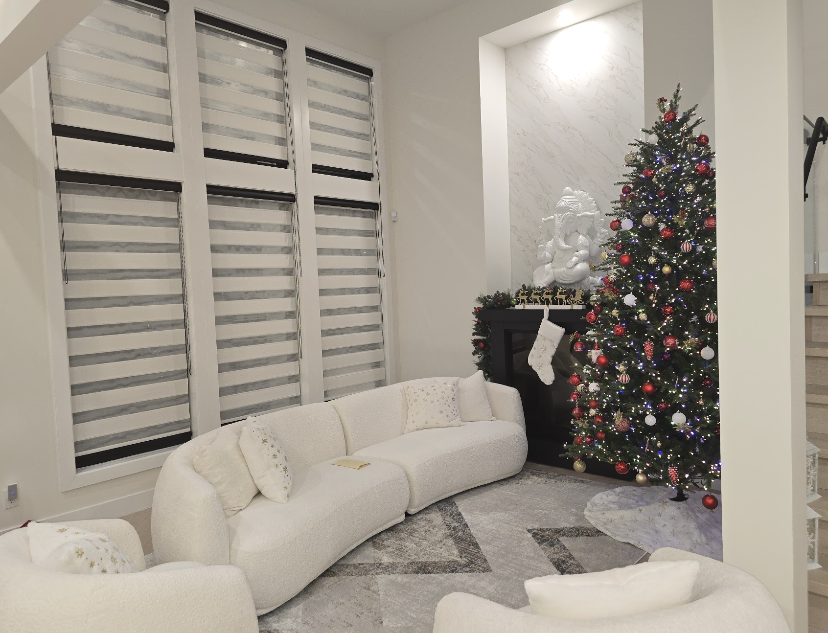 Living room decorated for Christmas with a white couch, a Christmas tree decorated with red and white ornaments, and a white statue of an elephant on the mantle above a fireplace.