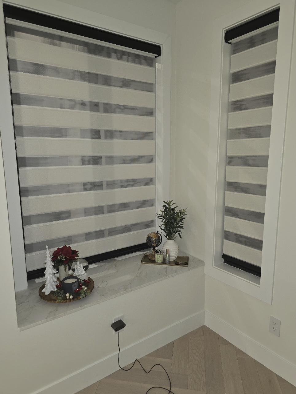 Decorative holiday display with Christmas ornaments, a poinsettia, and small Christmas trees on a marble window sill, next to a potted plant.