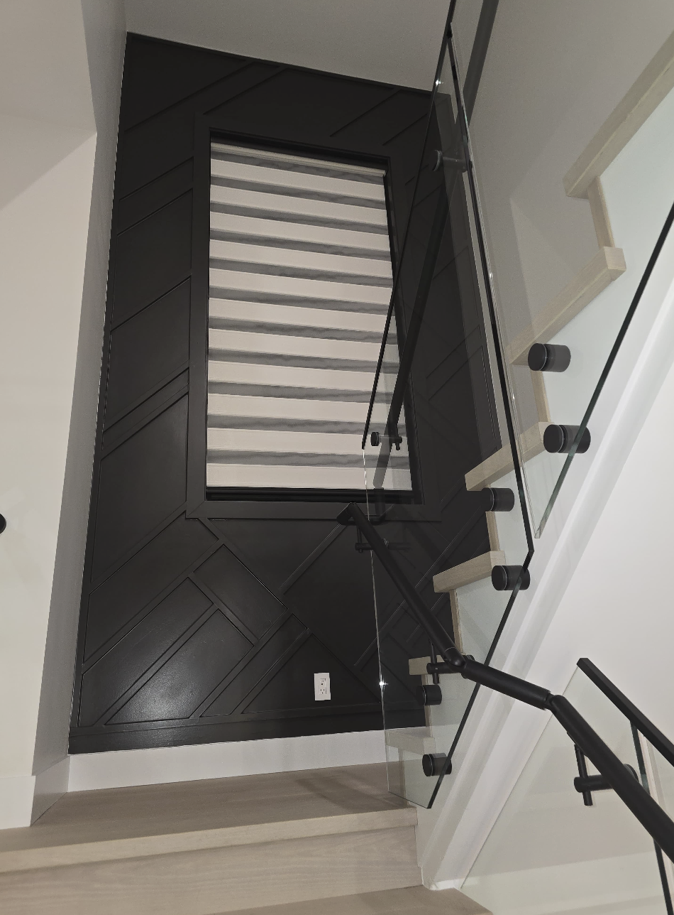 Top view of a staircase with black wall paneling, glass railing with black hardware, and white steps with gray anti-slip strips.