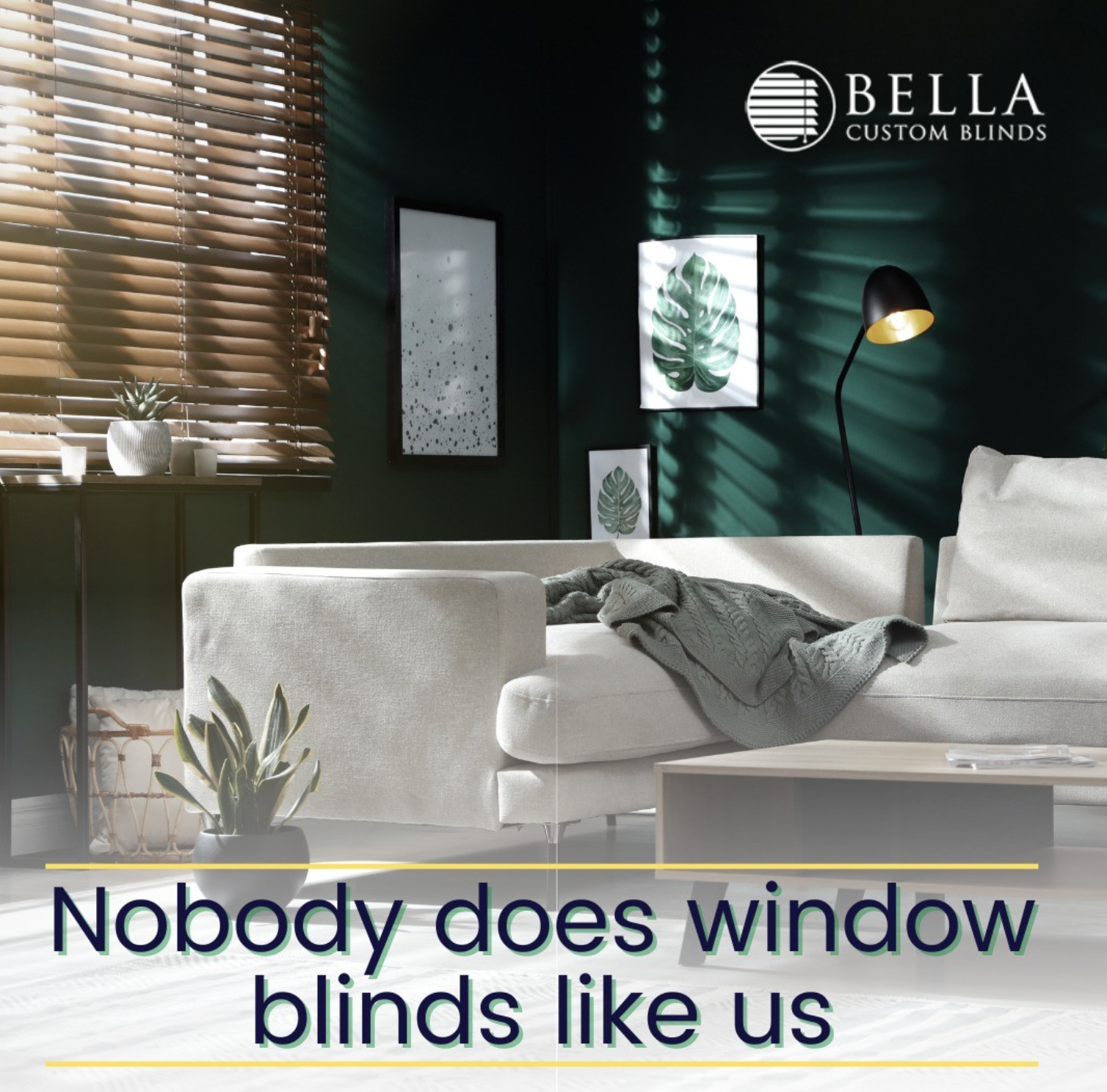 Living room with green wall, white sofa with blanket, window with blinds letting in sunlight, wall art with leaf images, houseplant, and a floor lamp, advertising Bella Custom Blinds.