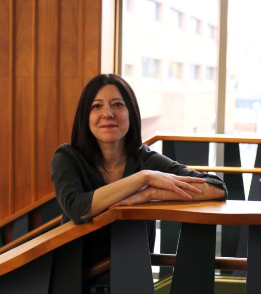 A woman with black hair standing on a staircase by a window in a room with wooden paneling.