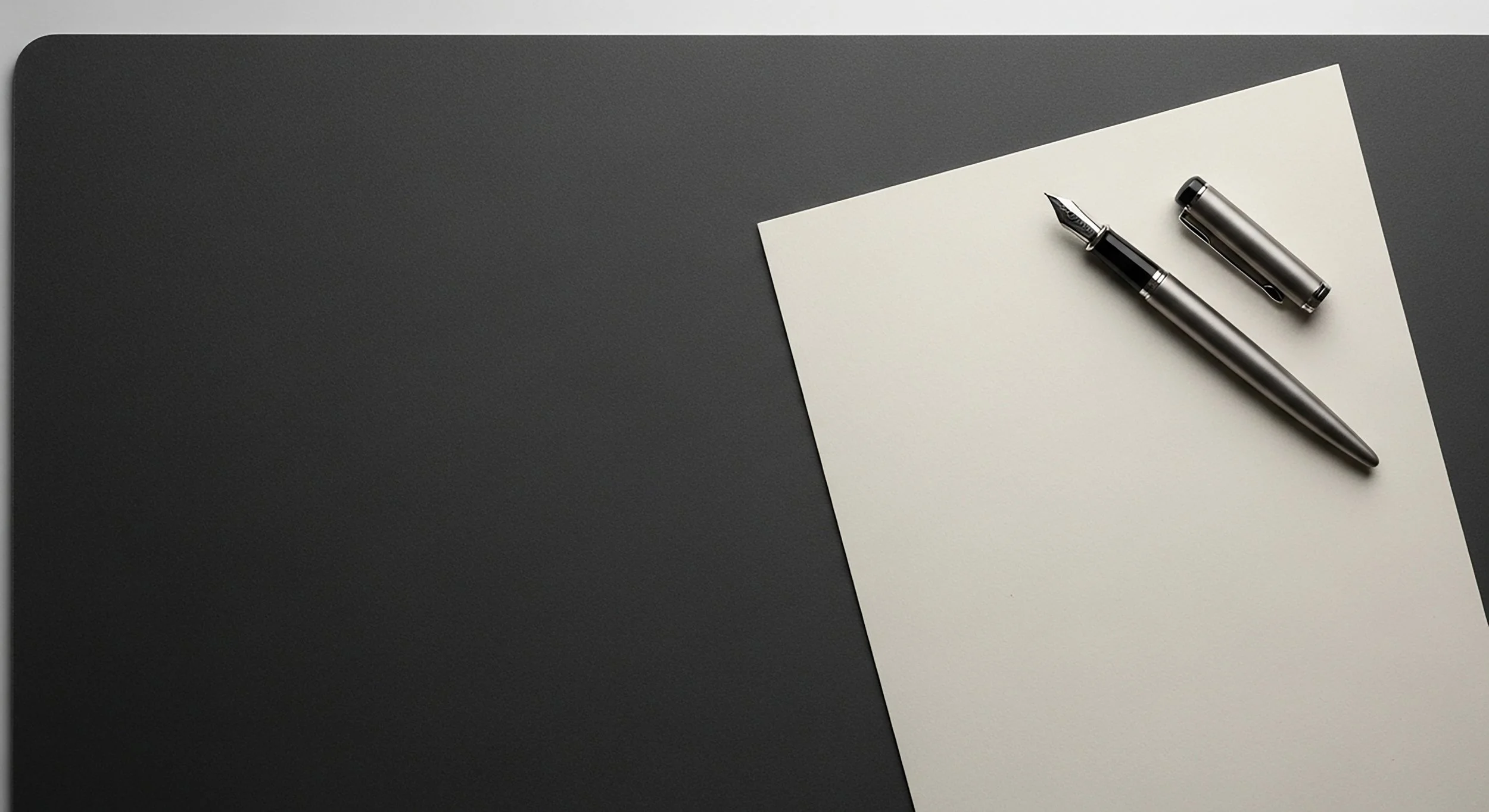 Pluma y capuchón sobre una hoja de papel sobre una mesa gris oscuro.