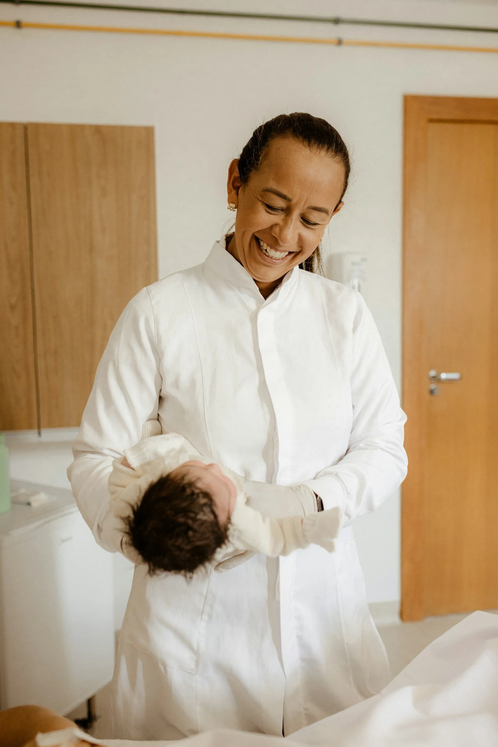 A young child with a towel over their head, lying on their stomach on a bed or soft surface, looking directly at the camera with a slightly puckered expression.
