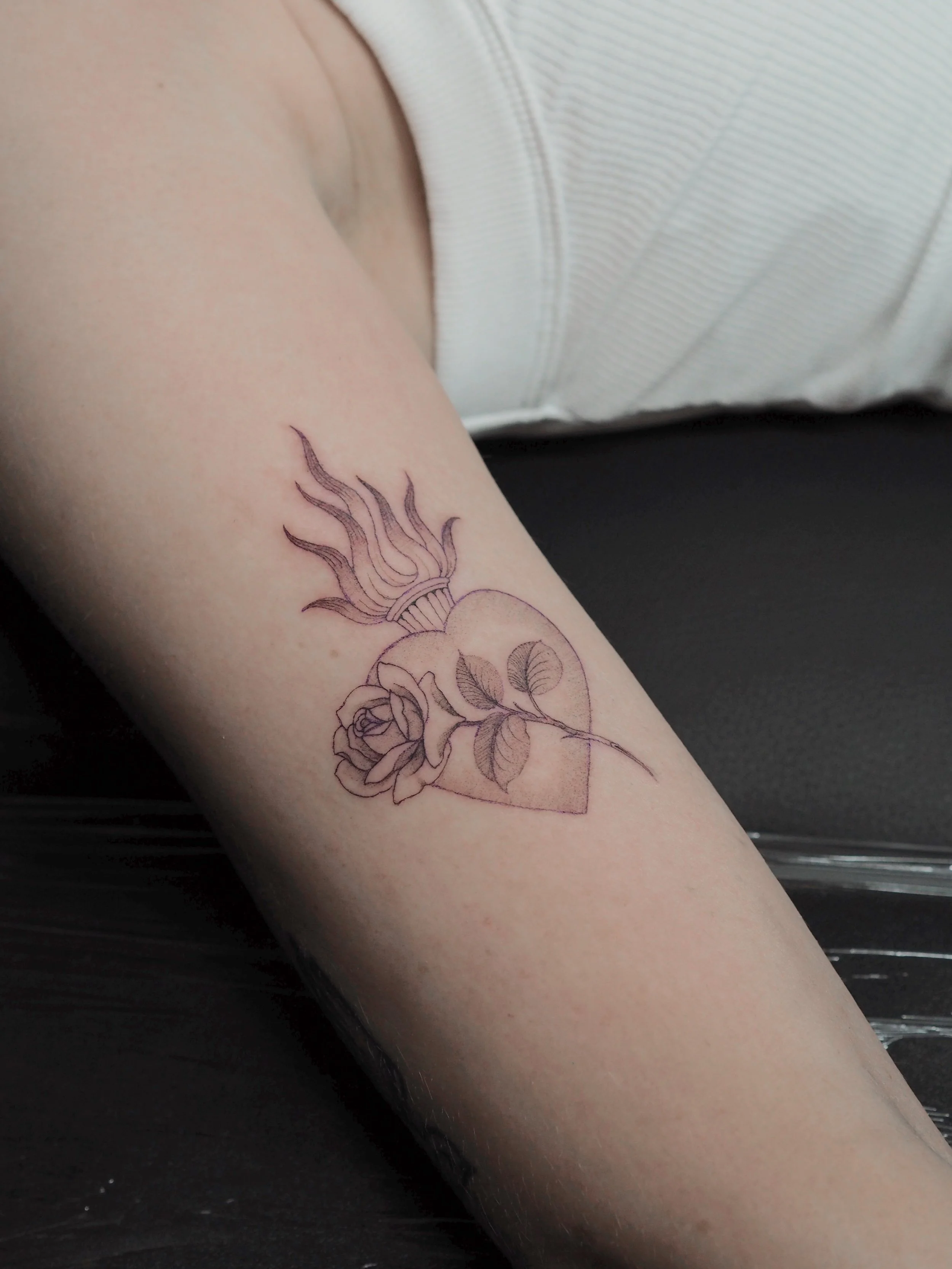Tattoo of a flame with a rose on a stem inside a hearton a person's arm.