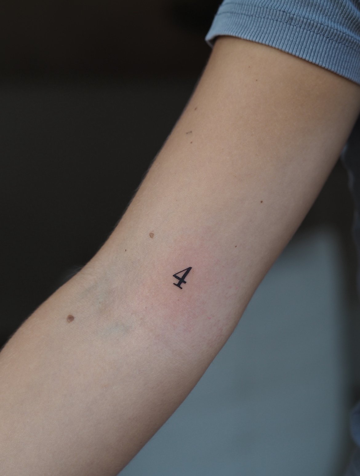 A close-up of a person's arm with a small black number four tattooed on the inner forearm.