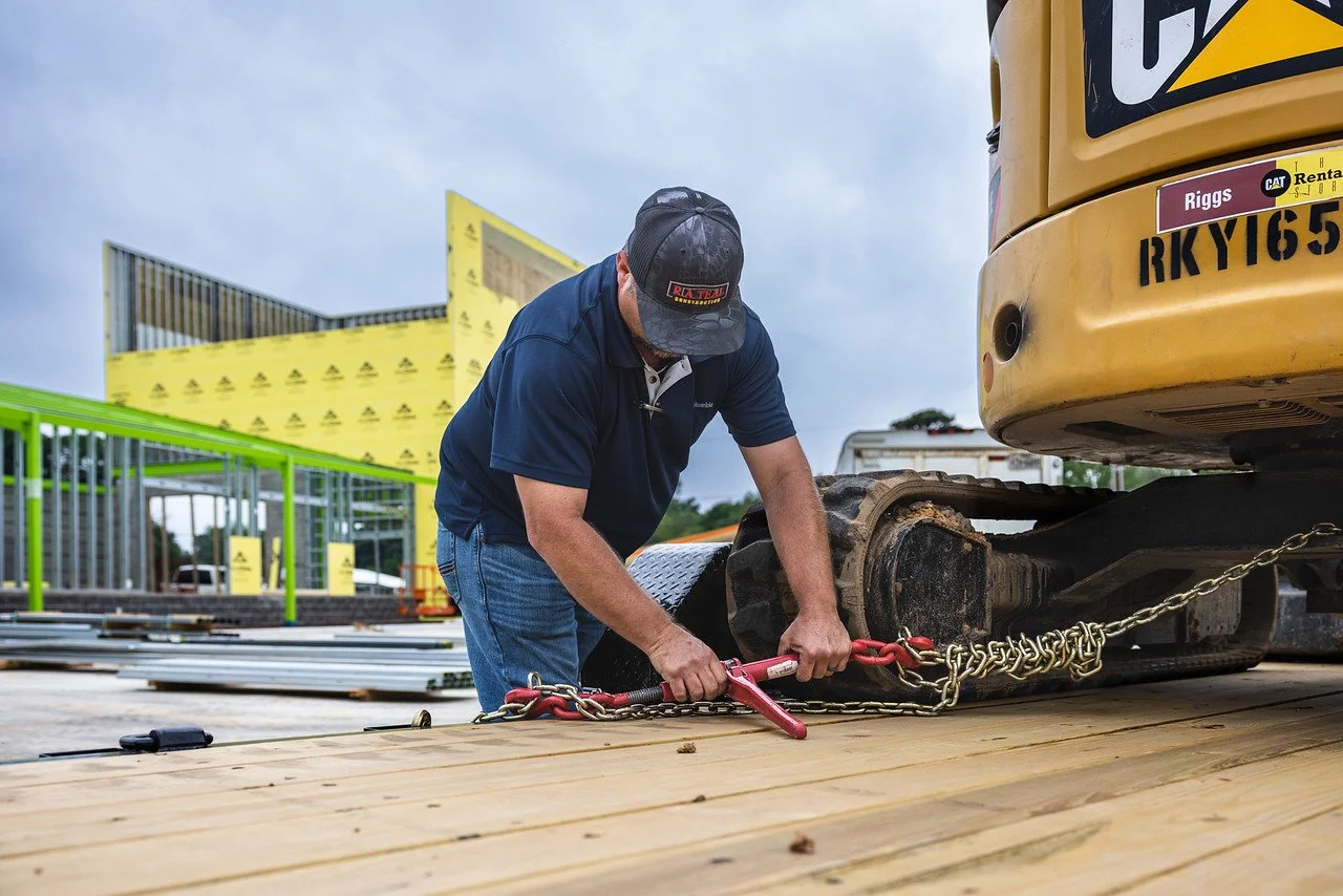 Construction worker securing a chainsaw to a construction vehicle on a wooden platform at a construction site.