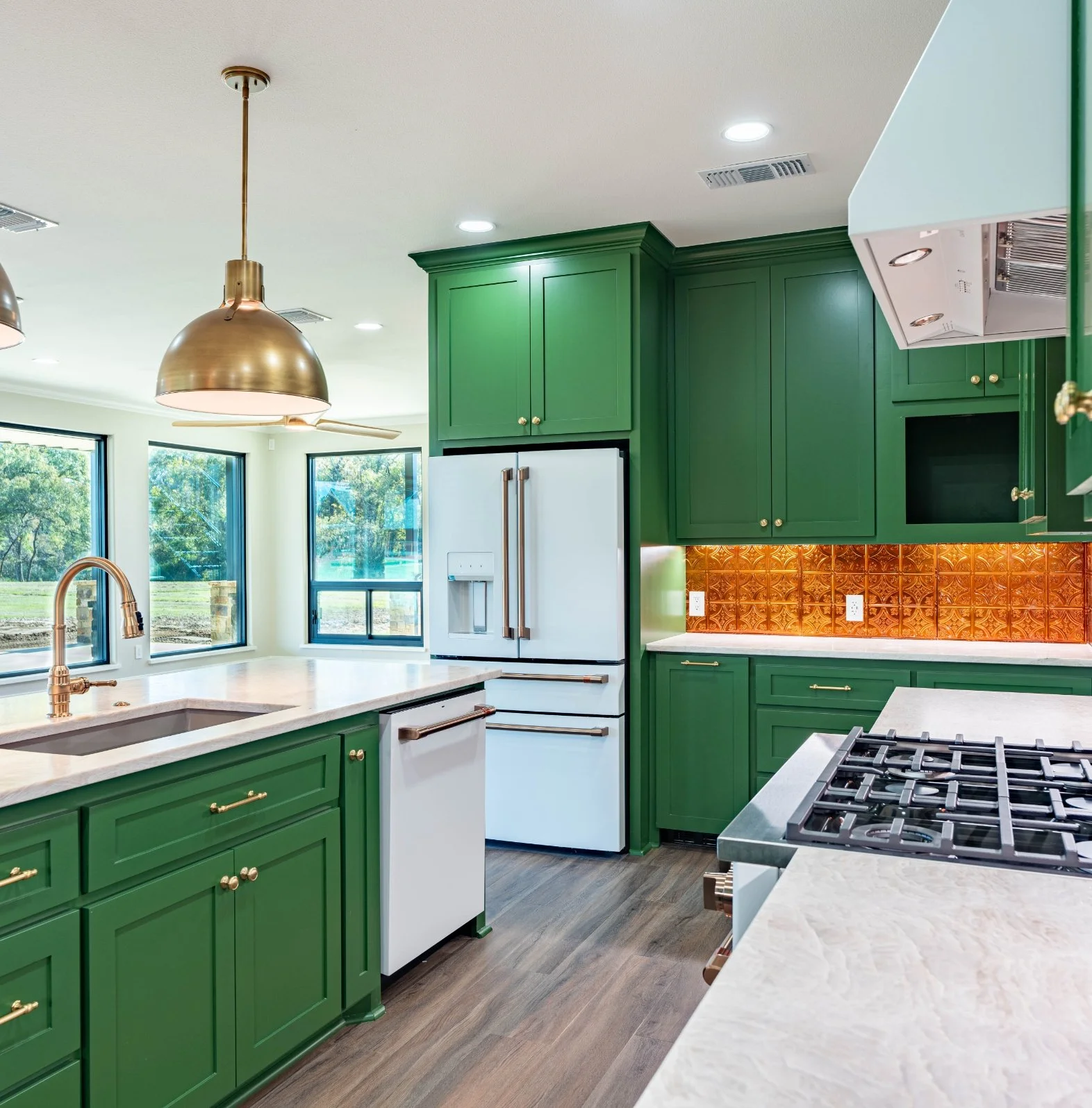 Modern kitchen with green cabinets, white countertops, large windows, stainless steel appliances, and dark wood flooring.