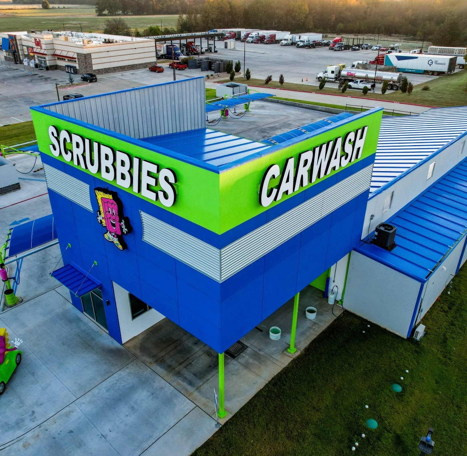 An aerial view of Scrubbies Car Wash building with signage and cartoon mascot, parking lot, and surrounding area.