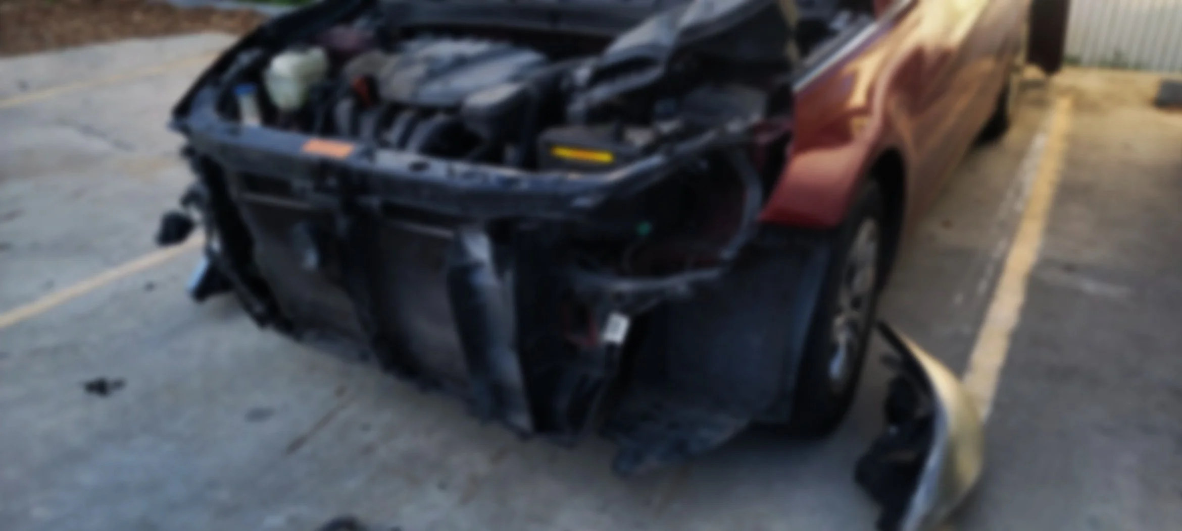 Blurry image of a destroyed red car with front end damage, parked in a parking lot.