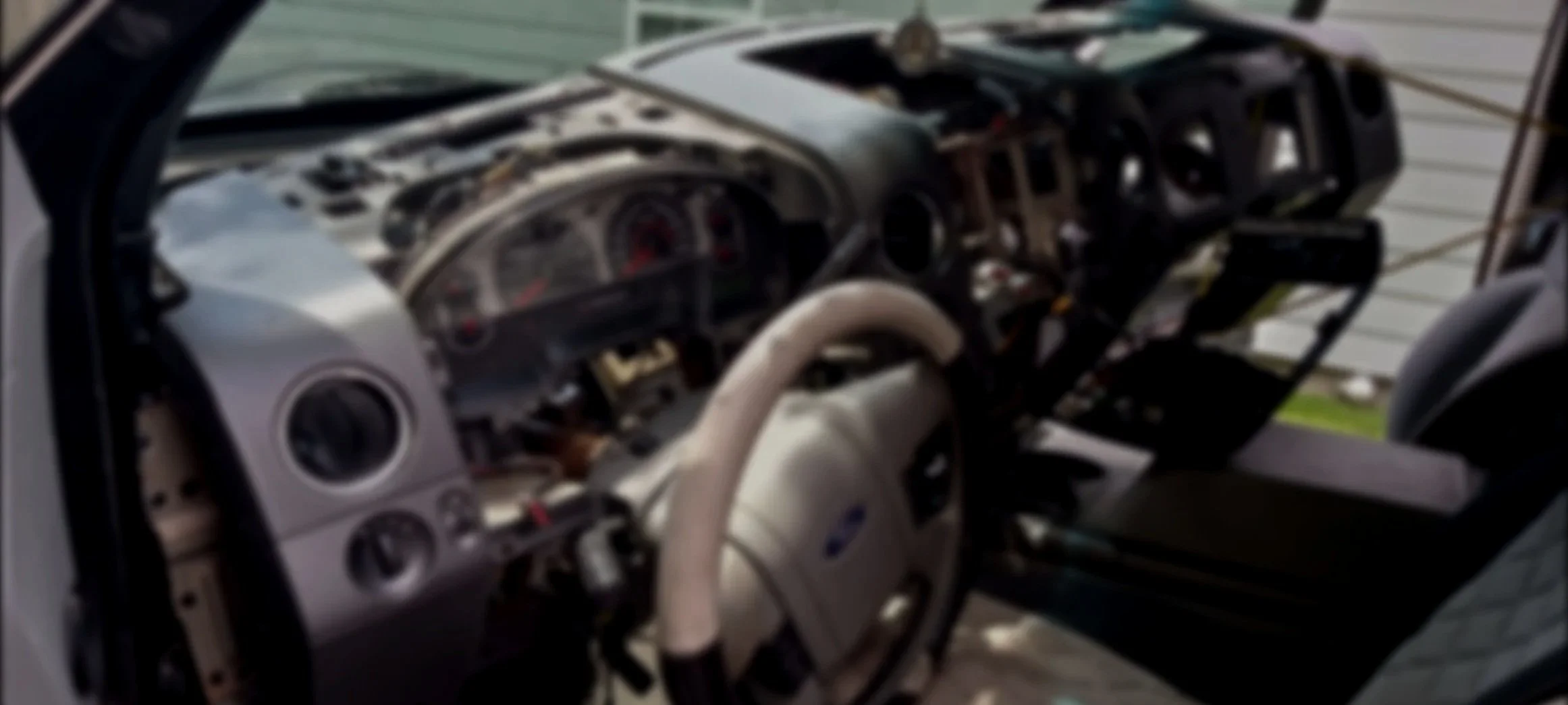 The interior of a vehicle with a damaged dashboard and missing components, showing exposed wiring and structural elements.