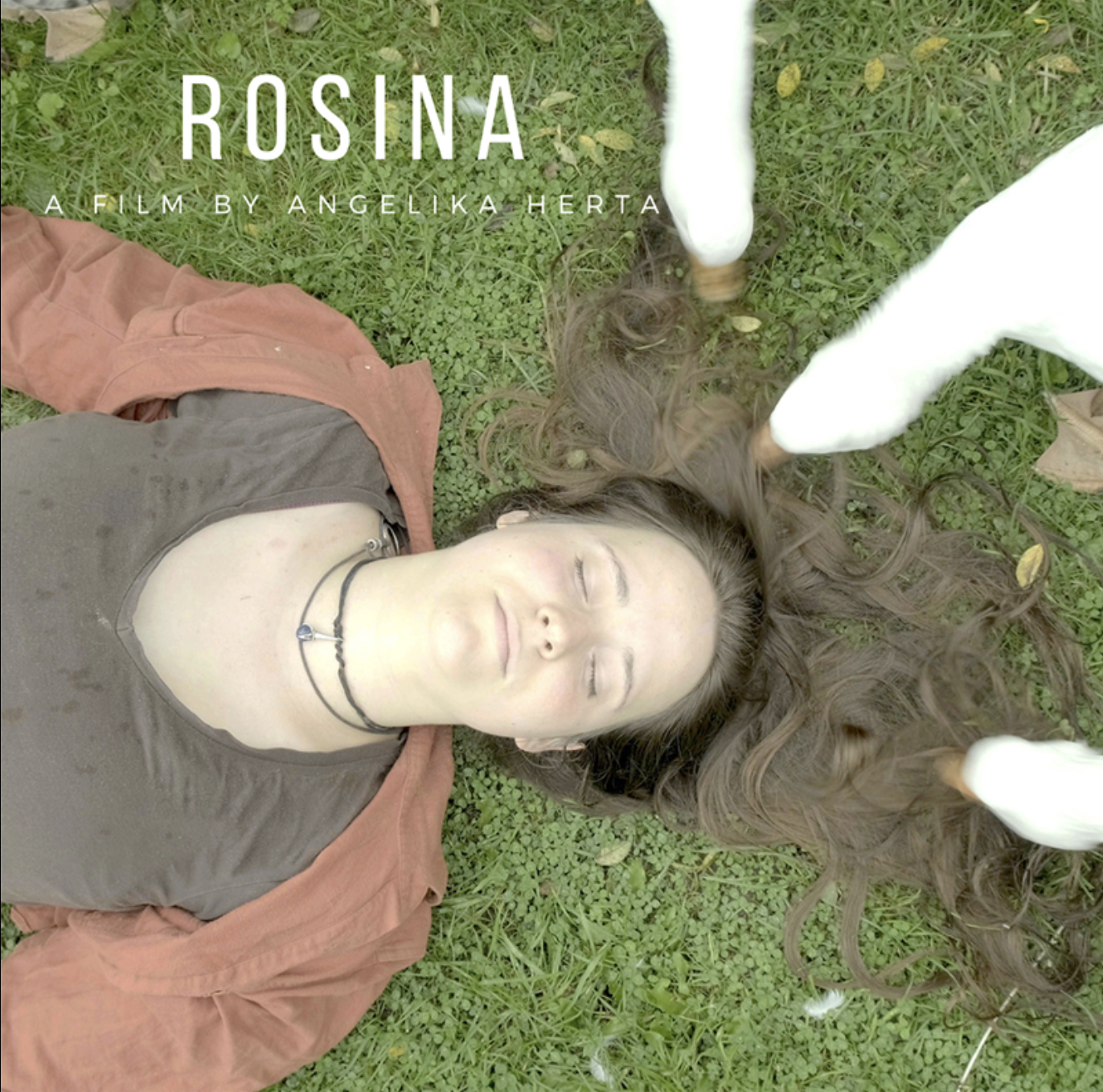 A woman with long brown hair lying on grass with eyes closed, surrounded by white feathers, wearing a brown shirt, an orange jacket, and a black choker.