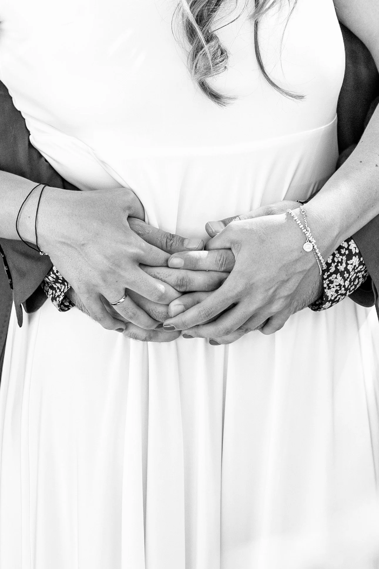 A black and white photo showing a couple with their hands intertwined over a woman in a white dress, likely at a wedding.