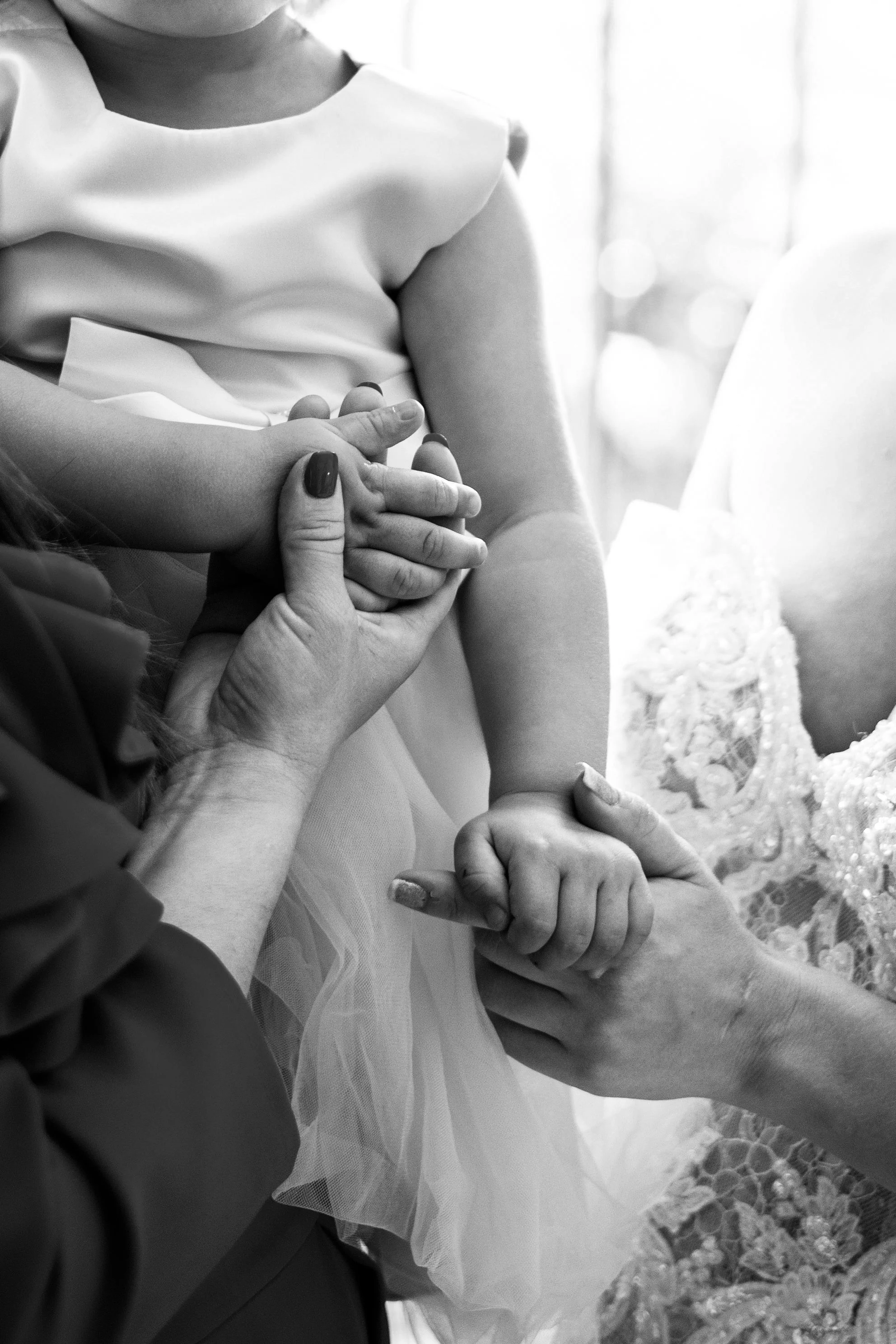 A child in a dress holding hands with an adult, with close-up of the hands, in black and white.