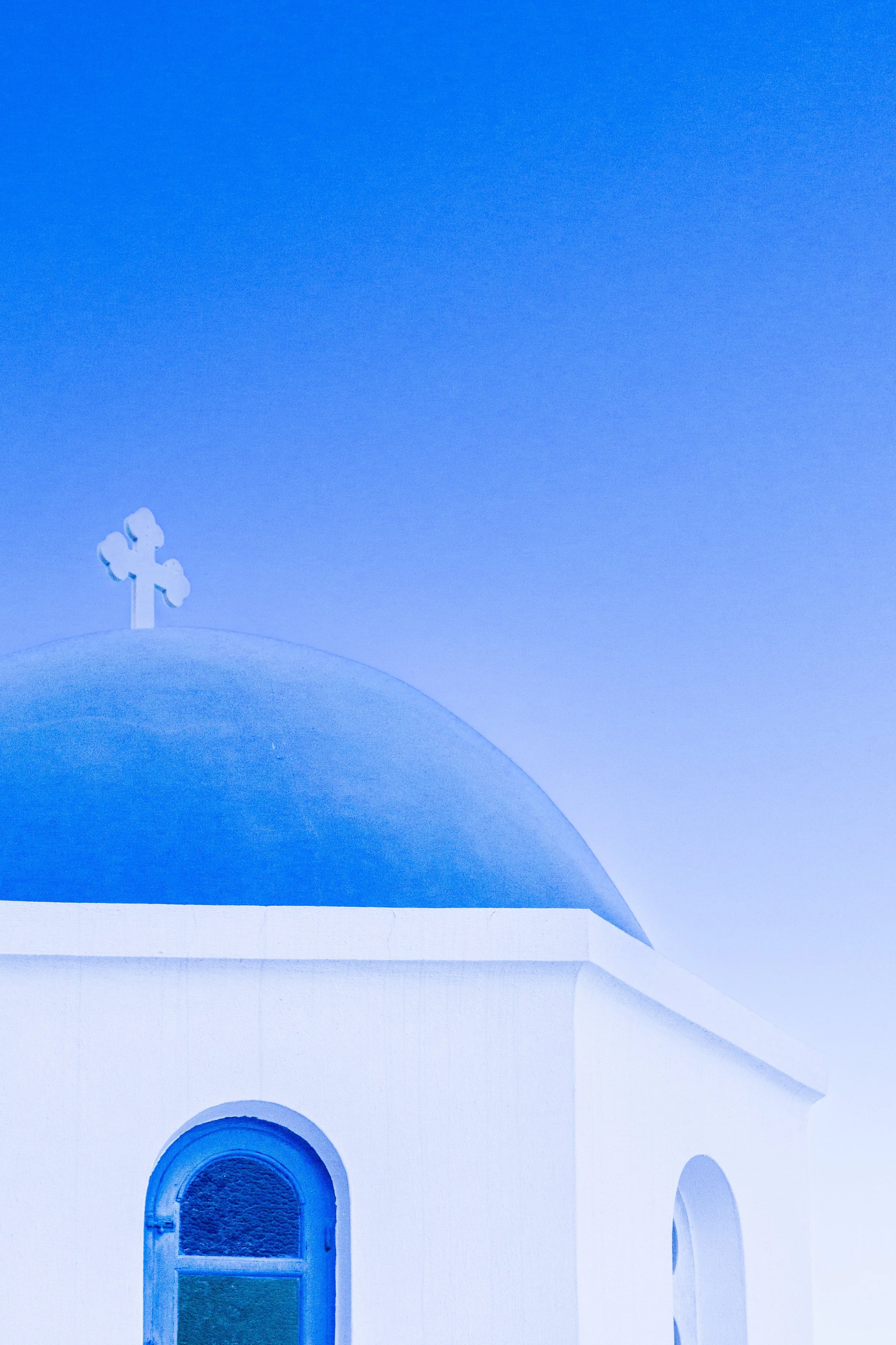 A white building with a blue dome and cross on top, characteristic of Greek Orthodox churches, under a clear blue sky.