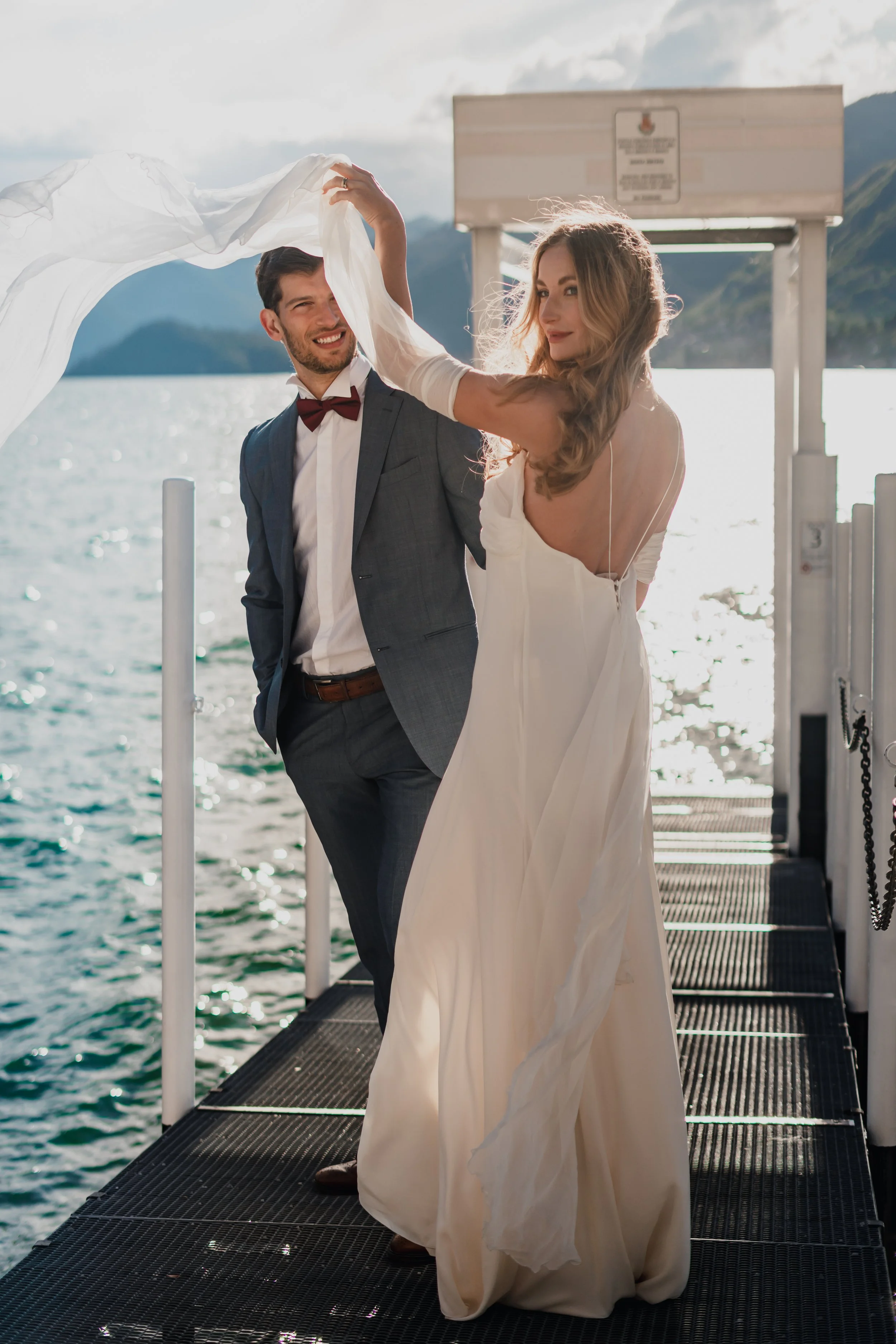 A bride and groom dancing on a dock by a lake, with mountains in the background, during a wedding celebration.