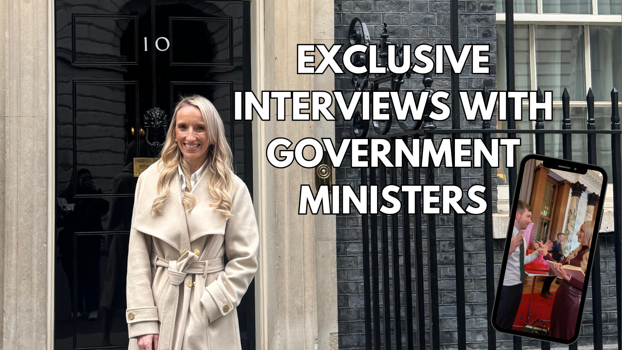 A woman with long blonde hair, wearing a beige coat, stands smiling outside the Black Door of 10 Downing Street in London, with bold text overlay reading 'Exclusive Interviews with Government Ministers' and a smartphone graphic showing a video call with two people in a formal setting.