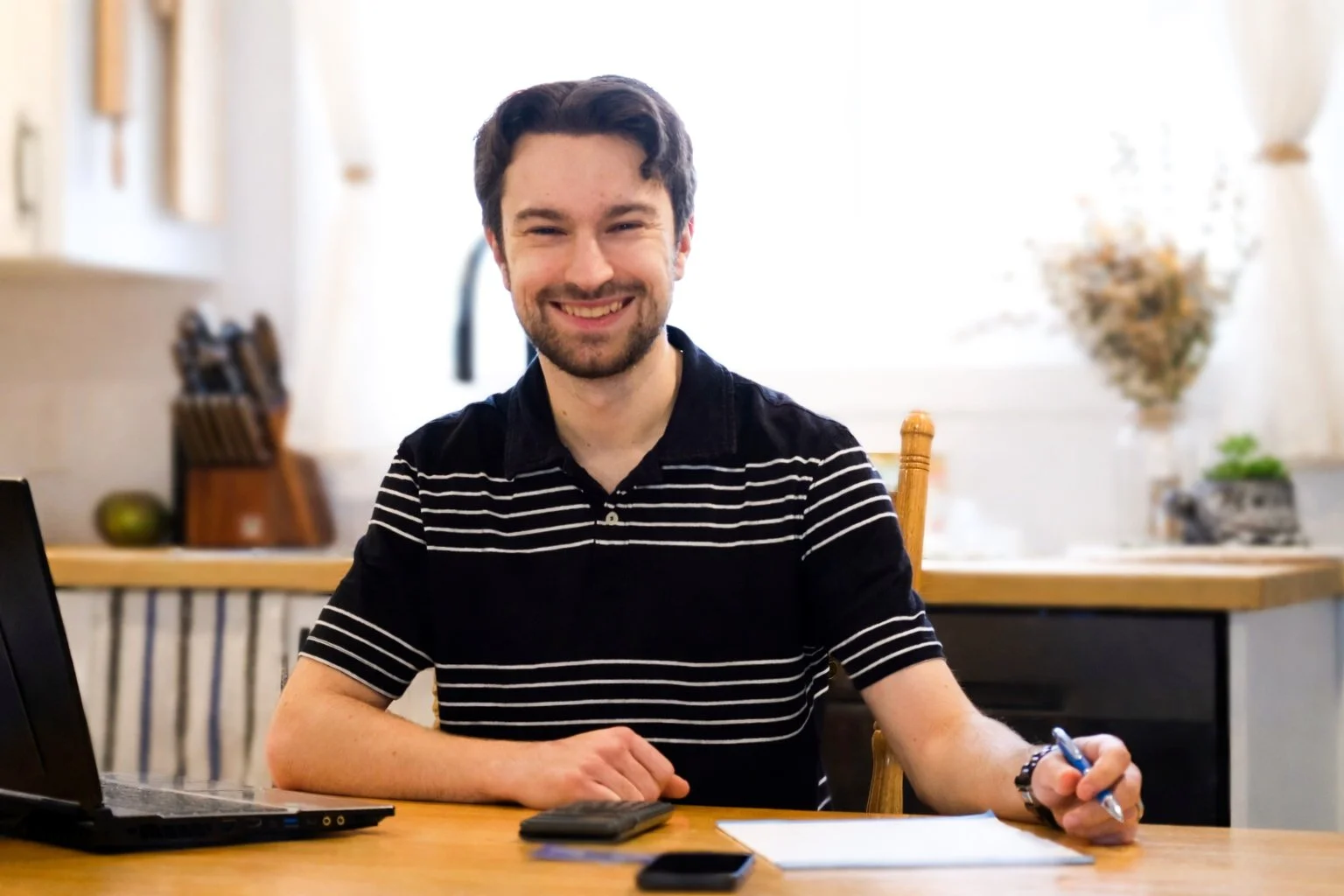 Portrait d’Anthony Hébert, technicien comptable, assis à son bureau avec un ordinateur portable et des documents, souriant dans un environnement de travail lumineux.