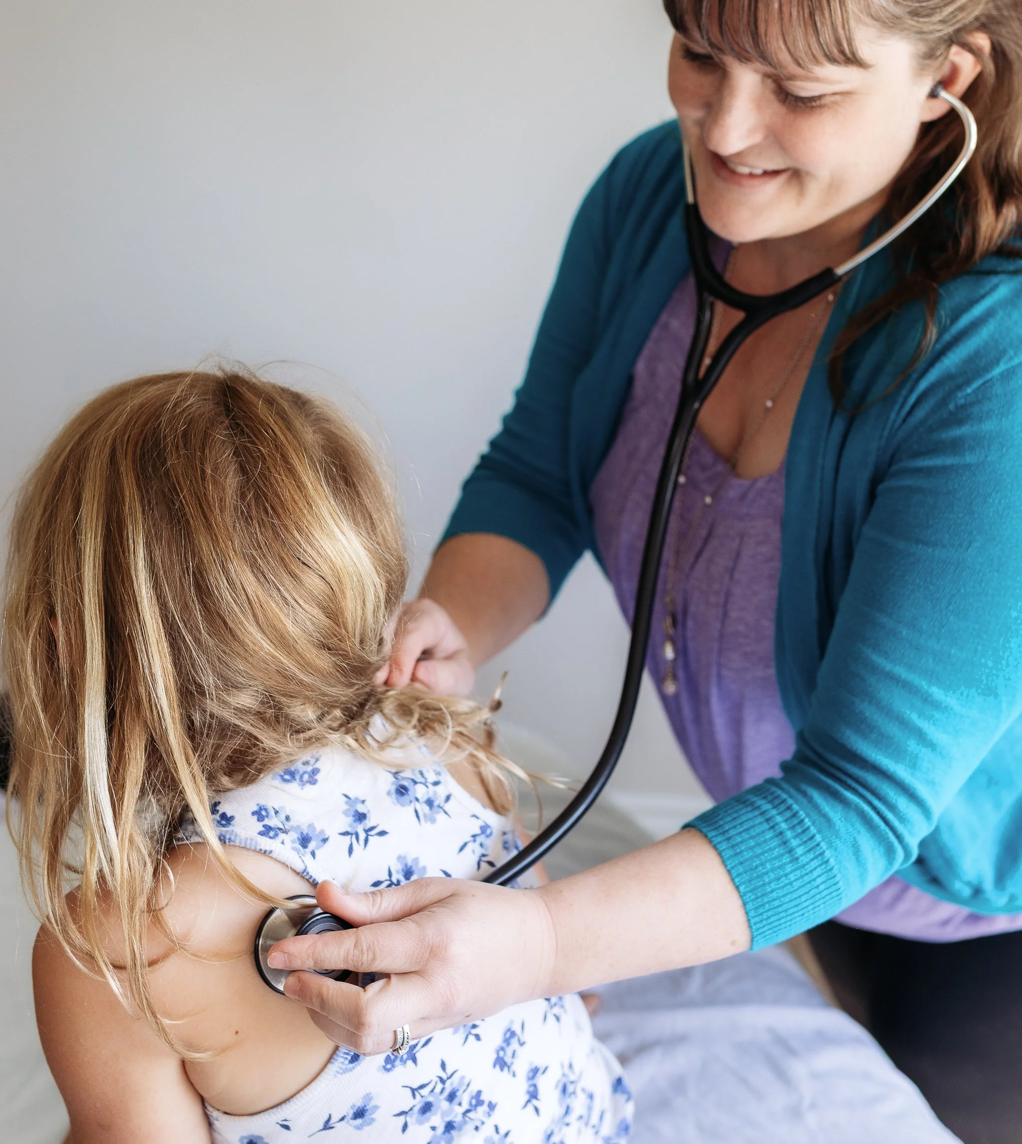 A healthcare professional listening to a young girl's chest with a stethoscope.