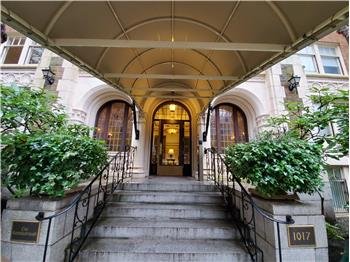 Apartment building entrance with stairs, potted plants, and an awning.