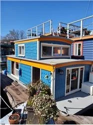Colorful tiny house with blue, yellow, and white exterior on a boat or floating platform.