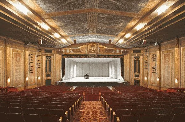 Empty theater with a stage and red seats, ornate gold and wood decor, and a grand ceiling.