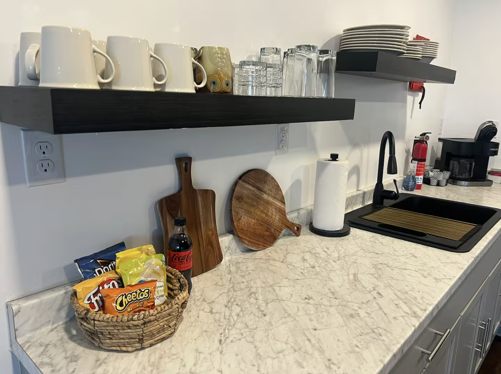 Kitchen countertop with snacks, cutting boards, paper towel, sink, and coffee machine.