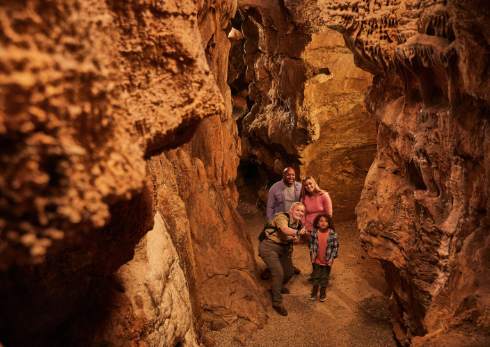 Four people, including two adults and two children, exploring a narrow, rocky canyon with tall, reddish-brown rock walls.