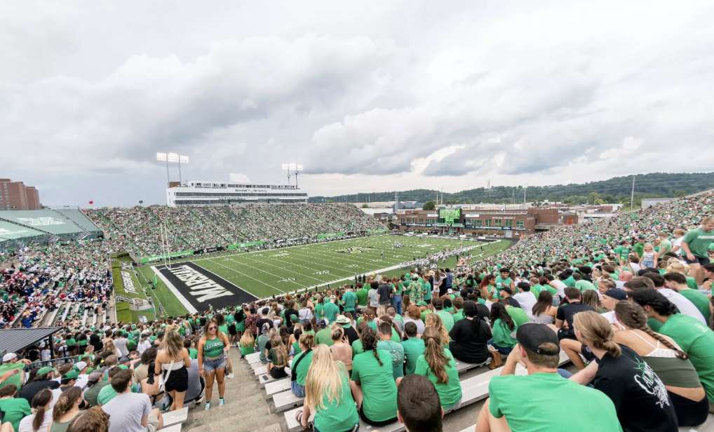 Crowd watching a football game at a stadium with cloudy skies.
