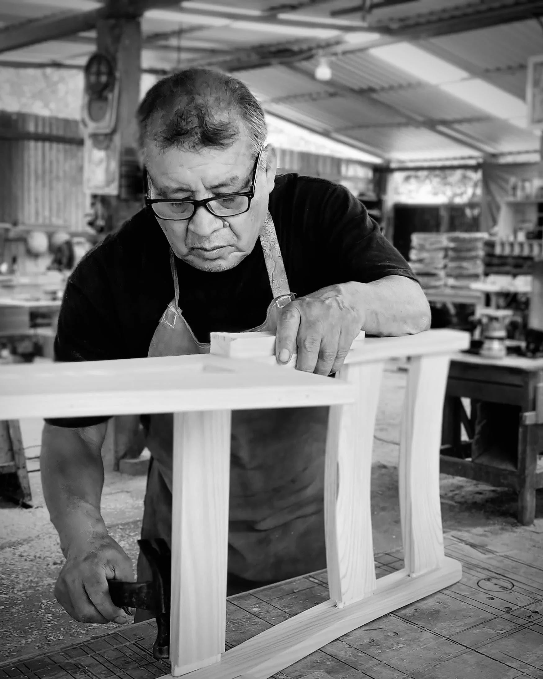 El Maestro Julio, fundador de Estudio Madera, trabajando artesanalmente una pieza de madera en Oaxaca. Un retrato que captura la maestría y el detalle técnico de 50 años de trayectoria en la carpintería de autor.