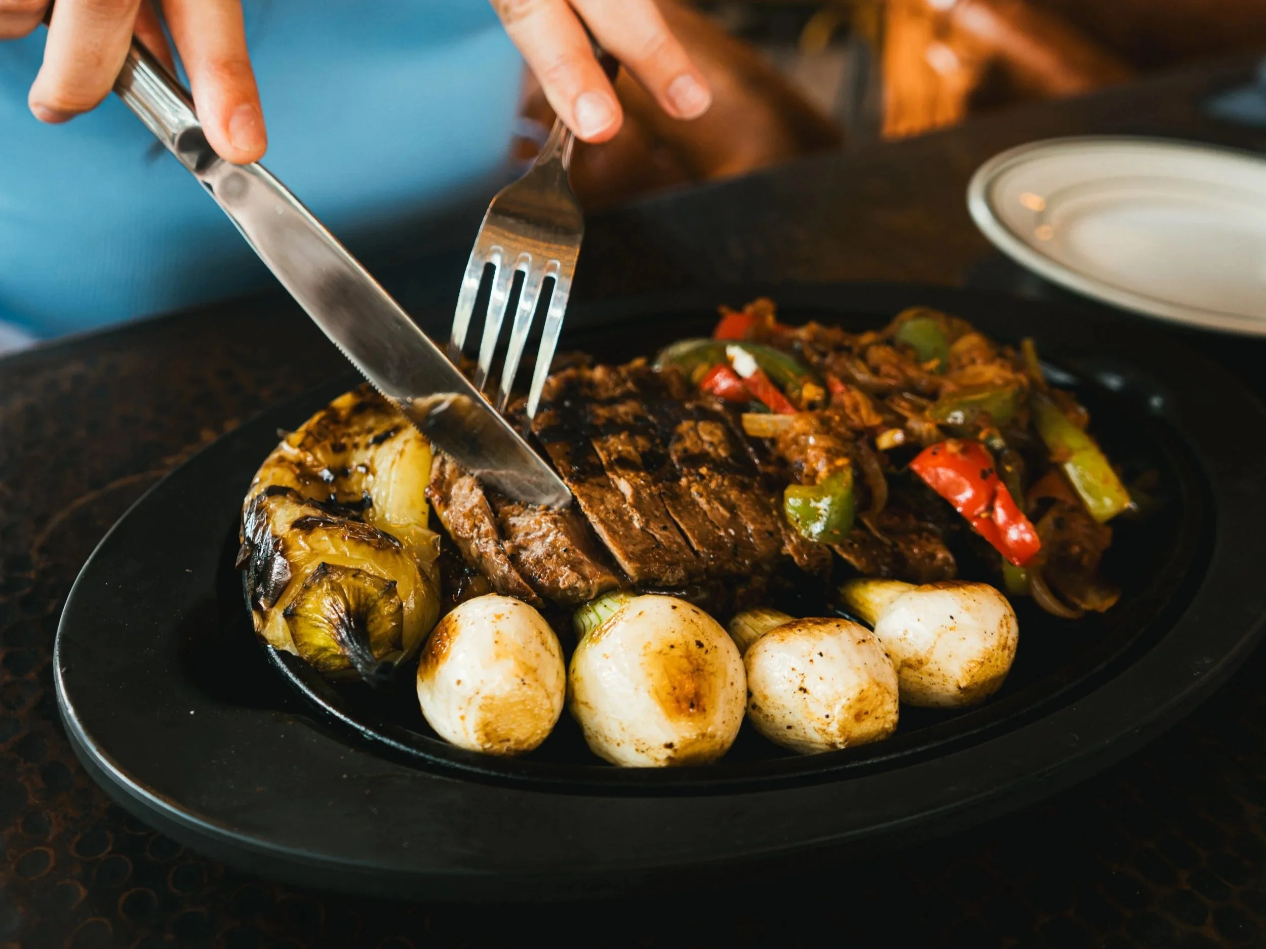 Person cutting grilled steak with vegetables and mushrooms on a black plate