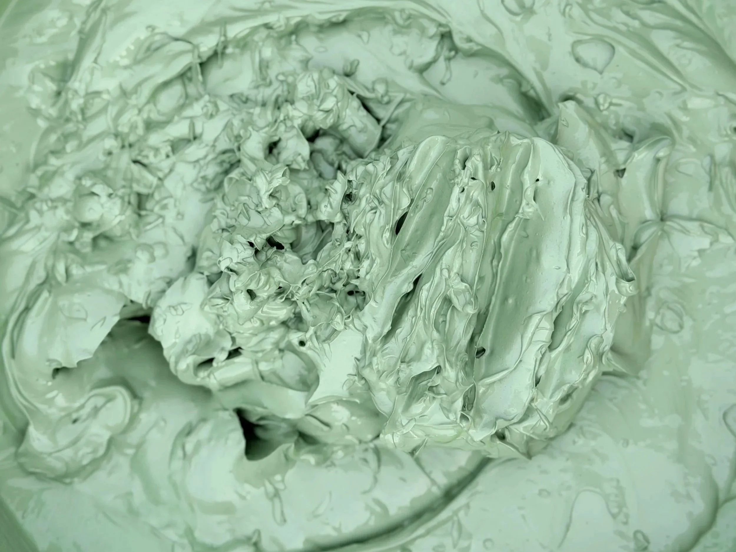 Close-up of a large mound of light green, whipped or spreadable substance inside a container.