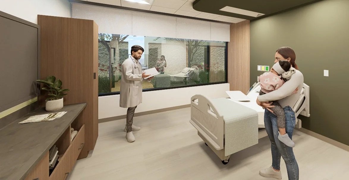 A hospital room with a healthcare professional standing near the window, talking with a woman holding a child. The woman is standing next to a hospital bed, and the room has a wooden cabinet, a small plant, and large window showing greenery outside.