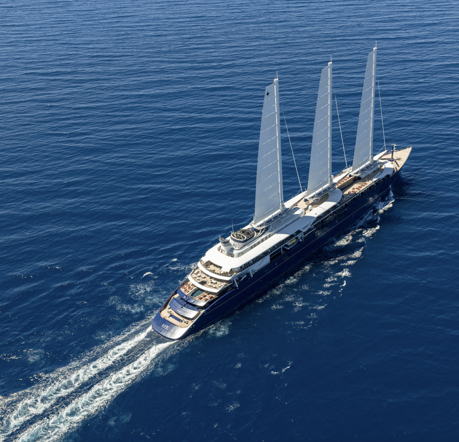 A luxury sailboat with three tall masts sailing on the open blue ocean.