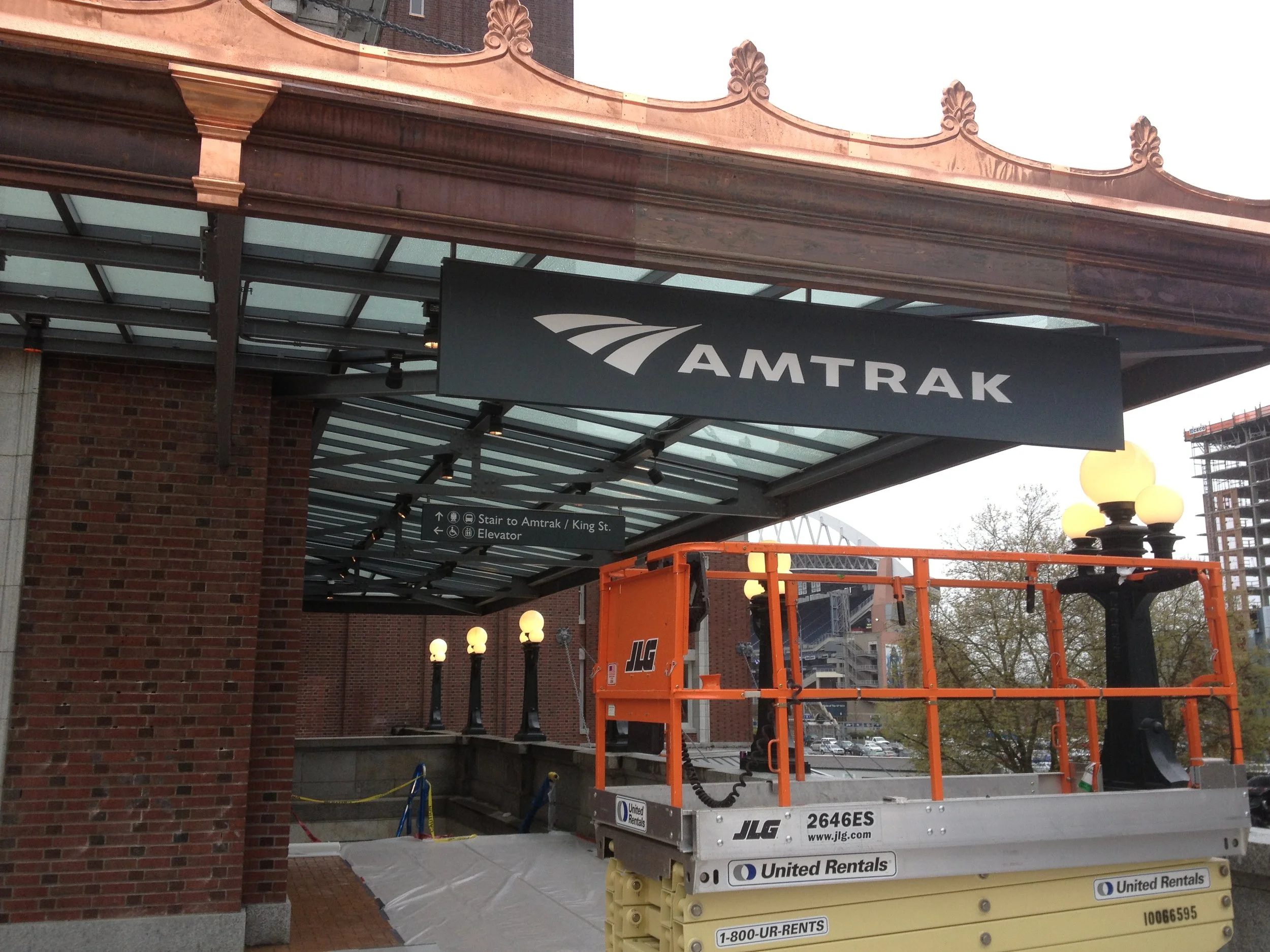 Construction lift in front of Amtrak station entrance with sign and illuminated lamps visible.