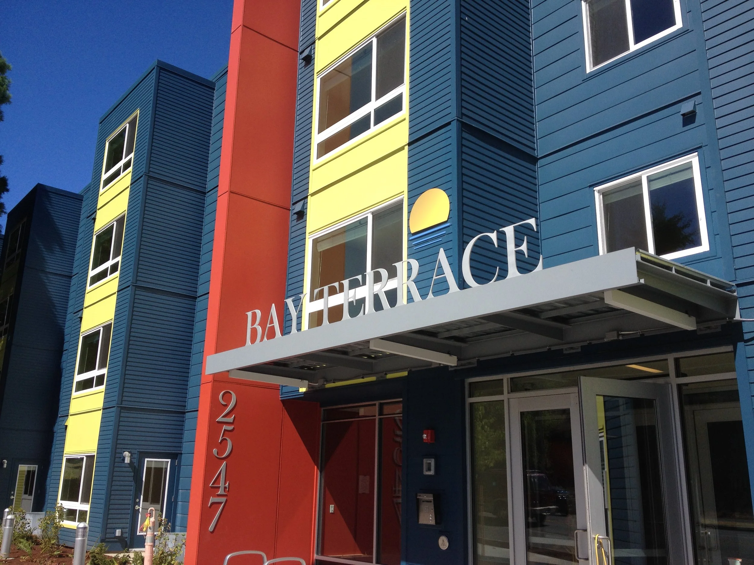 Colorful modern apartment building with blue, yellow, and red panels and a sign that reads 'Bay Terrace' above the entrance.