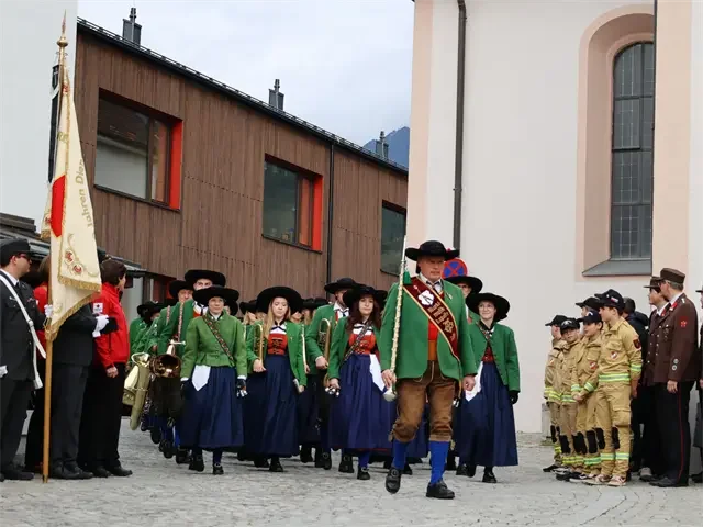 Eine Gruppe von Menschen in traditionellen Trachten bei einem Umzug oder festlichem event in einer Stadt. Manche tragen spezielle Uniformen, andere traditionelle Kleider.