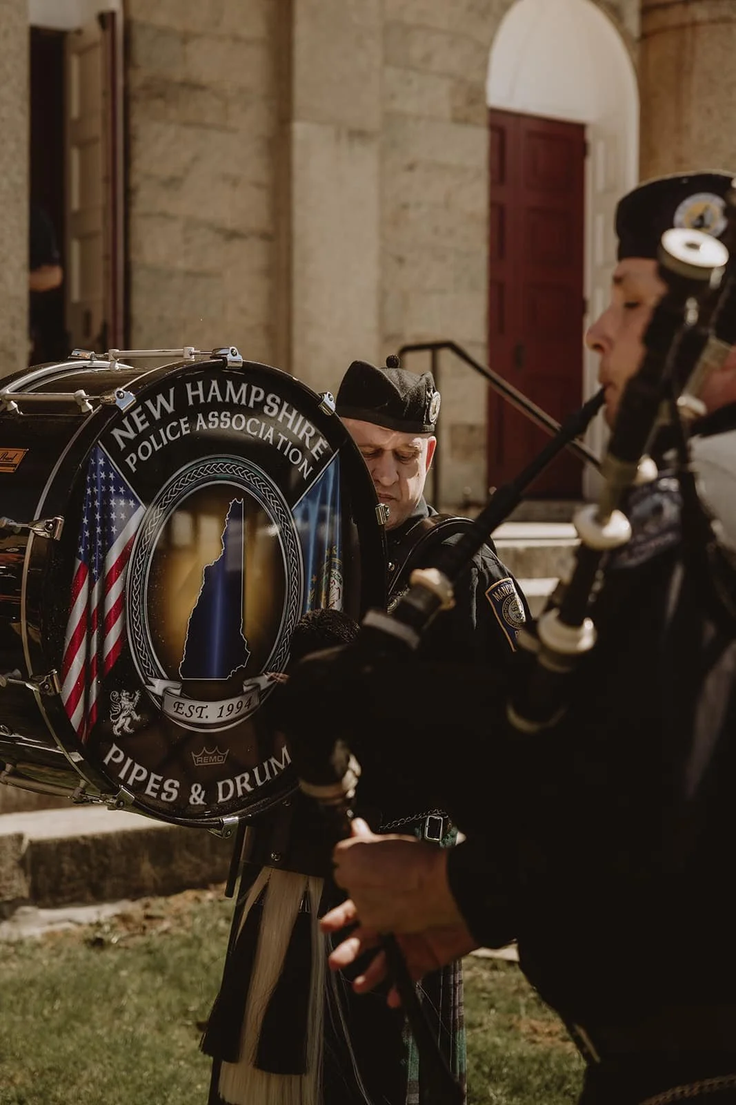 Police officers with a drum from the New Hampshire Police Association outdoors in front of a stone building.